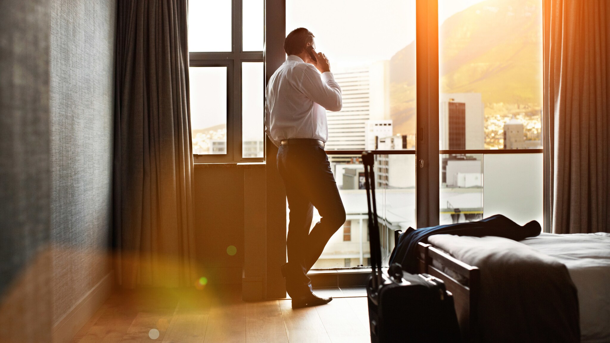 Geschäftsmann steht am Fenster eines Hotelzimmers und telefoniert.
